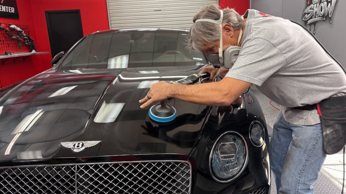 Mel Craig machine-polishing the hood of a black Bentley at The Recon Pros
