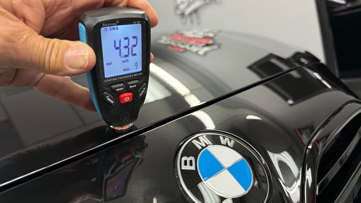 Coating thickness meter reading 4.32 mils on the hood of a black BMW
